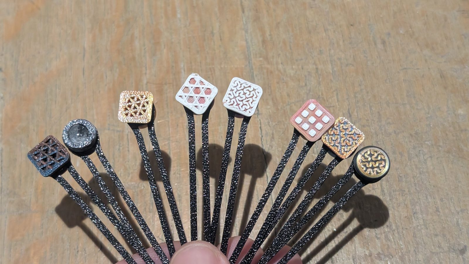 L'atelier — Neuf motifs de boutons montés sur leurs bras, ouverts en éventail pour être comparés d'un geste