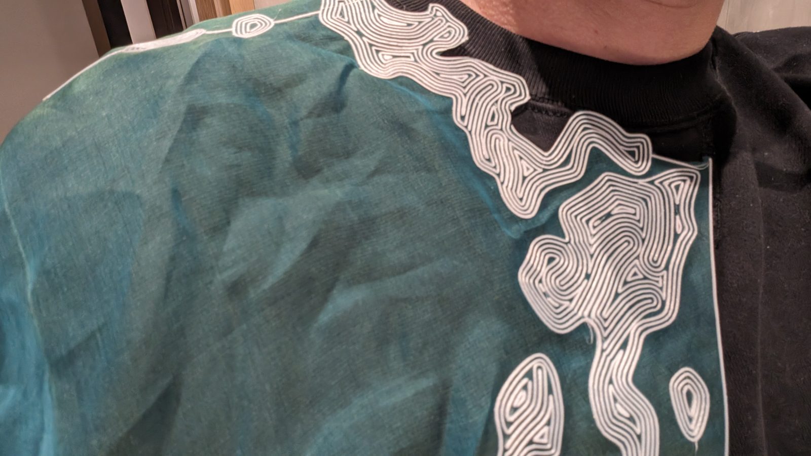 Re-former le textile — De près : la ligne franchit la couture de l'épaule sans s'interrompre, et le bord droit arrête le motif net